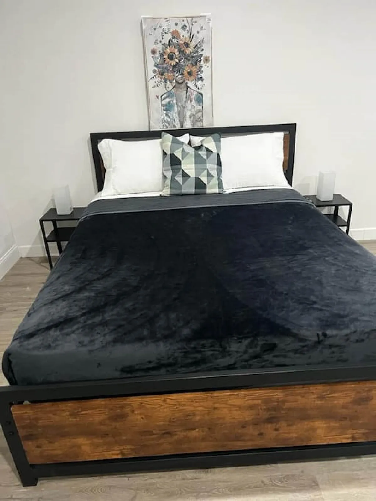 A cozy studio interior featuring a neatly made bed with vibrant pillows, artistic wall decor, and soft, natural lighting. The space appears inviting and peaceful, ideal for relaxation and personal downtime.